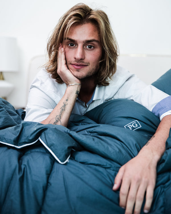 Man lying in bed under a blue comforter with 'PG' branding