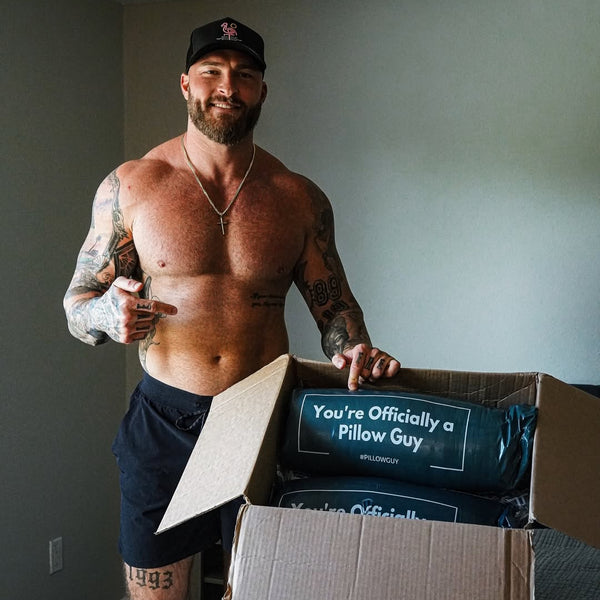 Man opening a box with a pillow inside, standing in a room.